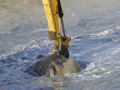 Excavator bucket dredging sand and gravel from the seafront